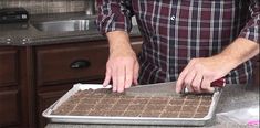 a man cutting up food on top of a cookie sheet in a kitchen next to a sink