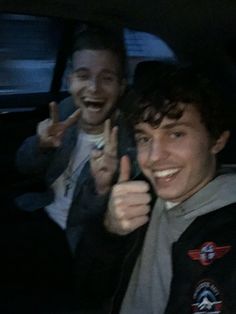 two young men sitting in the back seat of a car giving thumbs up while smiling