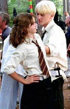 two young people standing next to each other in front of a group of people wearing white shirts and ties