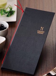 a black menu cover sitting on top of a wooden table next to a bowl of olives