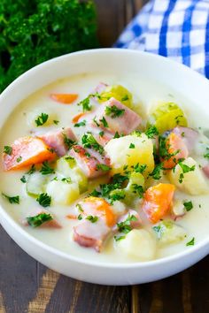 a white bowl filled with potato and ham soup on top of a wooden table next to parsley