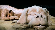 a woman sitting next to a fake dog on top of a rocky ground with it's mouth open