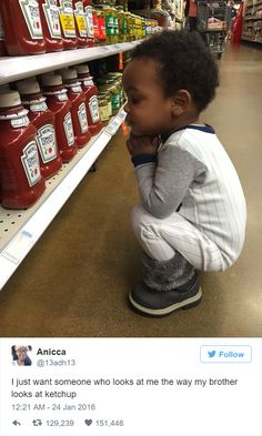 a little boy sitting on the floor in front of a shelf with ketchup bottles