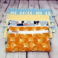 three zippered pouchs are lined up on a wooden surface, one is orange and the other is blue