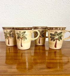 four coffee cups with palm trees painted on them sitting on a wooden countertop in front of a white wall