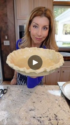 a woman holding up a pie crust in front of her face on the kitchen counter