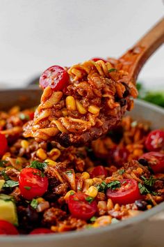 a spoon full of food with tomatoes, corn and other vegetables in it is being lifted from a skillet