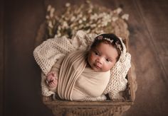 a baby wrapped up in a blanket laying on top of a wooden crate with flowers