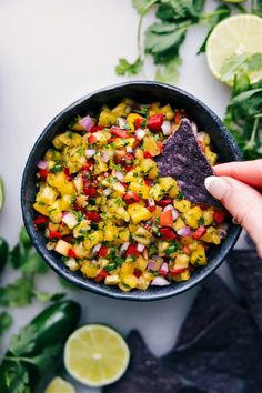 a hand holding a tortilla chip over a bowl filled with salsa and cilantro