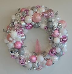 a pink and silver christmas ornament wreath hanging on a wall next to a tree