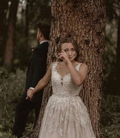 a woman in a wedding dress standing next to a tree with her hand on her face