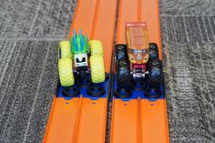 two toy trucks are sitting on top of orange track boards, with blue wheels and yellow tires