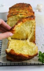 a person holding a loaf of bread on top of a cooling rack with parsley