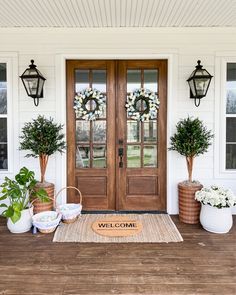 two potted plants sit on the front porch of a white house with wooden doors