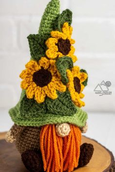 a crocheted gnome hat with sunflowers on it sitting on top of a tree stump