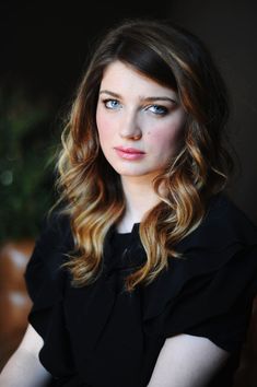 a woman with long hair and blue eyes sitting in a chair looking at the camera