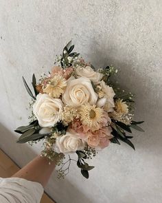 a bridal bouquet is being held by someone's hand in front of a wall