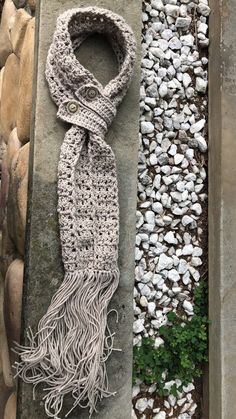 a knitted scarf sitting on top of a stone slab next to a pile of rocks