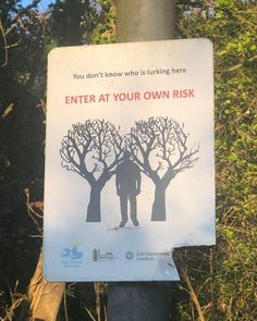 a sign posted on a pole in front of some trees with the words enter at your own risk