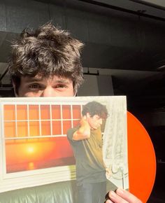 a young man holding up an orange record with the image of a boy on it