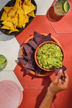 a person holding a tortilla chip in front of a bowl of guacamole