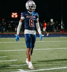 a football player is walking on the field with his hands in his pockets and wearing blue gloves