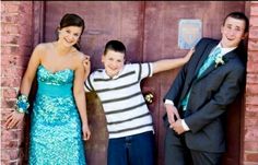 three people standing next to each other in front of a brick wall with one person wearing a suit and tie