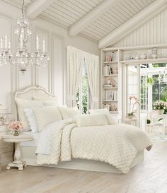 a white bedroom with chandelier, bed and window in the corner is shown