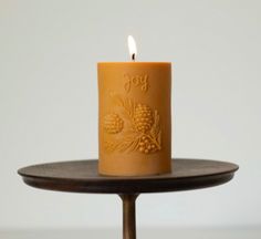 a lit candle sitting on top of a wooden table next to a plate with a pine cone