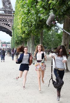 three young women are running down the street in front of the eiffel tower