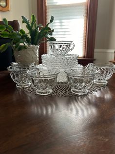 a set of glass dishes sitting on top of a wooden table next to a potted plant