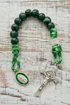 a green beaded bracelet with a silver cross on it and a charm that says jesus