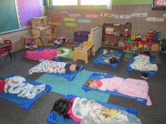 there are many children sleeping in small beds on the floor at this school room's desks