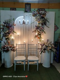 two white chairs sitting next to each other in front of a wall with flowers on it