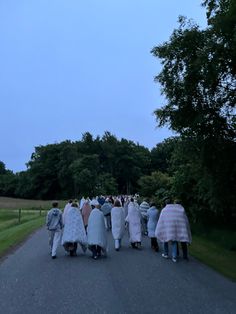 a group of people walking down a road in the middle of a park at dusk