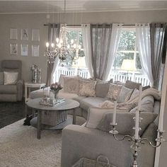 a living room filled with furniture and a chandelier hanging from the ceiling in front of two windows