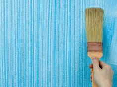 a person holding a paint brush in front of a blue wall with vertical stripes on it