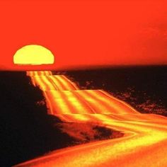 the sun is setting over an empty road in the middle of the ocean with light streaks on it