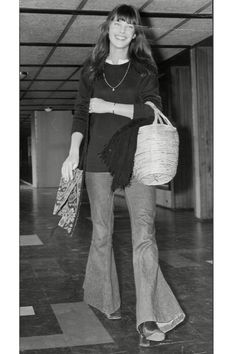 an old photo of a woman holding a basket and wearing flarey jeans, smiling