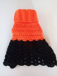 an orange and black crochet hat is laying on a white surface