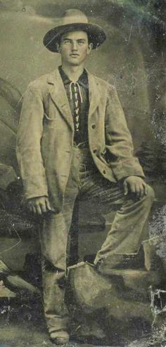 an old photo of a man in a suit and hat standing next to a rock