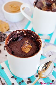 two white mugs filled with chocolate cake on top of a blue and white table cloth