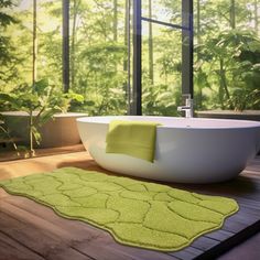 a bath tub sitting on top of a wooden floor next to a green rug in front of a window