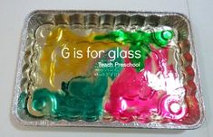 there is a metal tray that has different colored plastic objects in it and the words g is for glass on it