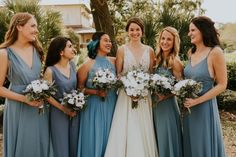 a group of women standing next to each other in front of trees and bushes holding bouquets