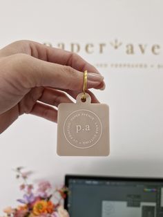 a person is holding a small square keychain in front of a computer screen