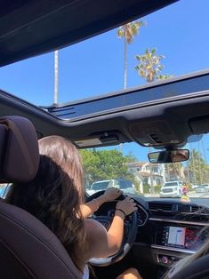 a woman driving a car with palm trees in the background