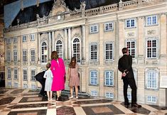 three people standing in front of a building with two children and an adult looking at it