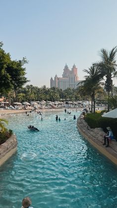 many people are swimming in the pool near palm trees and hotels on the other side