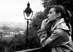 a woman standing next to a lamp post on top of a hill near a city